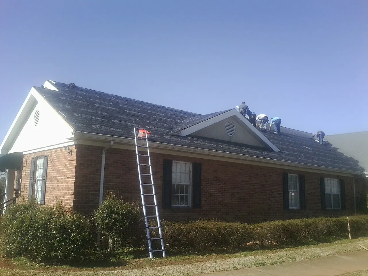 Crew tearing shingles off a brick ranch roof with a ladder set — Metal Roof Repair work by our crew in Boiling Springs